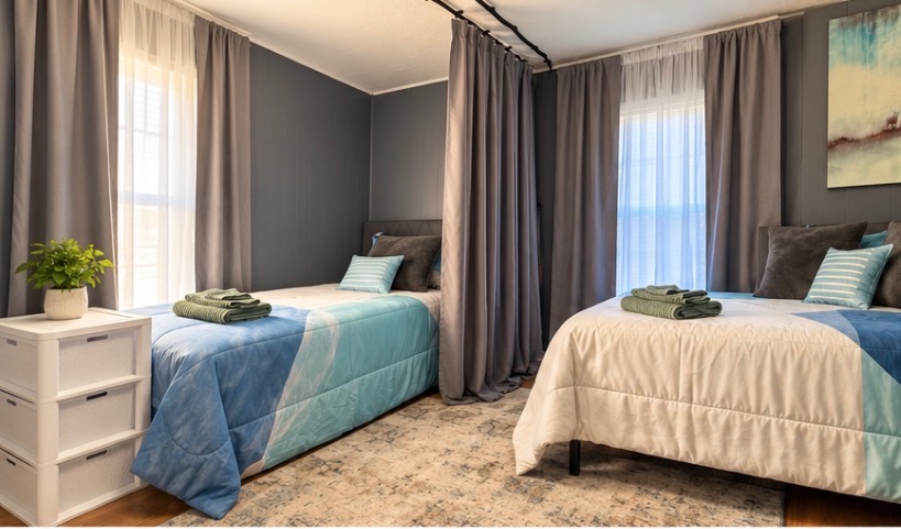 Shared bedroom with two made beds, fresh towels and a privacy curtain between them